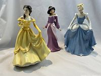 Front view of the three Royal Doulton Disney princess figurines: Belle in yellow dress, Jasmine in purple dress, and Cinderella in blue dress.