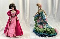 Both Barbie dolls pictured side by side on stands showing full outfits and size reference with green apple