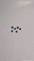 Six small square cut London blue topaz gemstones laid out on a light background, showing size variation and quality of cut.