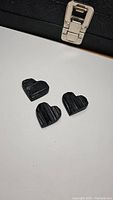 Three small hand carved untreated black tourmaline heart-shaped stones displayed on white background with a black case behind them.