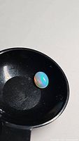 Oval cabochon Ethiopian opal gemstone shown against black background. Displays bright multicolored flash with dominant blue, green, and orange hues.