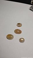 Four oval cabochon golden rutilated quartz gemstones arranged on white background showing varying sizes and inclusions.