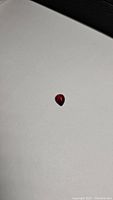 Photo of a pear-shaped cherry red garnet cabochon gemstone on a white background, showing its size and color.