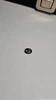 Clear close-up photo of the oval cut green sapphire on a white surface, showing gemstone color and shape.