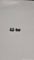 Two rectangular green tourmaline gemstones on a plain background, highlighting their cut, color, and clarity.