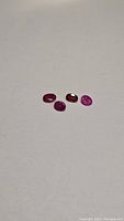 Four natural rubies in varying shades of pink and red laid on a white surface showing size and translucency differences.