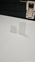 Two natural selenite stones, one square and one rectangular, standing upright with a black case in the background.