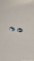 Two pear shaped sky blue topaz gemstones placed side by side on a light surface, showing clarity and color