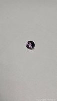Close-up photo of loose round cut purple amethyst gemstone on white background.