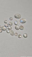 Parcel of multiple oval and round cabochon rainbow moonstones laid out to show size variation and blue flash.