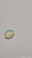 Close-up photo of 1.24ct oval cabochon Ethiopian opal showing multicolored flashes on a light background.