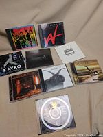 Photo of the full lot featuring nine CDs from various rock and cult classic artists, arranged on beige fabric.