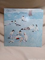 Front cover of 'Blue Moves' album showing painted artwork of people lying on grass under a tree.