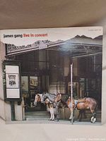 Front cover of the James Gang Live in Concert vinyl record showing urban scene with three saddled horses.