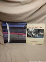 Album and accompanying book 'Hands Across The Water - Wings Tour USA' photographed together on fabric backdrop.