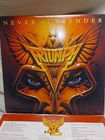 Front cover of 'Never Surrender' vinyl album by Triumph showing bold eagle graphic and band name, with lyric insert partially visible below.