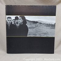 Front cover of U2 The Joshua Tree vinyl album in black with band photo on the cover showing four band members in a desert landscape.