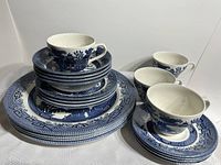 Front angle overview of stacked Blue Willow pattern teacups, saucers, small bowls, and plates.