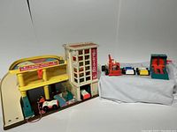 Front view of Fisher-Price parking garage playset, yellow ramp, elevator tower, and included toy vehicles in worn condition.