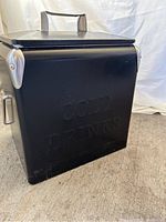 Side view of the black metal cooler showing embossed "COLD DRINKS" text and silver corner protectors.