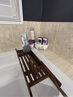 Bathtub with wooden slatted tray resting across it along with bath accessories on the corner.