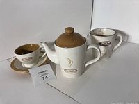 Photo showing Tim Hortons ceramic teapot with brown lid, tea cup with saucer, and coffee cup with Tim Hortons logos