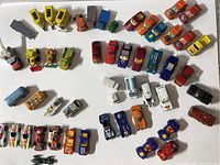 Top-down view of a collection of various 1970s diecast toy cars and vehicles showing a wide assortment of colors and models arranged on a white surface.