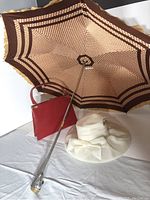 White vintage wide-brimmed hat, red purse, and umbrella with brown geometric pattern opened, showing ruffled edge and metal handle.