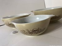 Three vintage Pyrex mushroom pattern nesting bowls stacked showing exterior design with mushroom and foliage decoration on cream background.