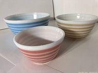 Three Pyrex nesting bowls side by side with blue, yellow, and pink stripes
