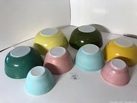 Two sets of four vintage Pyrex nesting bowls shown upside down revealing the solid pastel and bold colors.