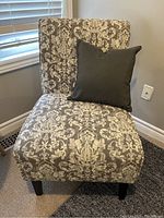Front view of the white and grey patterned fabric accent chair with dark grey pillow on it, showing cushioned seat and backrest, and wooden legs.