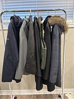 Seven women's jackets and coats hung on a rack, side view showing different colors and styles including a Columbia branded navy coat.