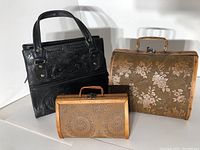 Black leather purse with embossed floral design sits behind two wooden purses with floral and circular carved patterns.