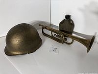 Photo of Canadian WW1/WW2 recycled helmet, brass horn, and fabric-covered water canteen together on white background.