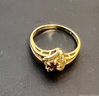 Ring viewed flat on a surface showing heart-shaped cluster with diamond accent and red gemstone.