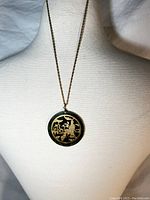 Full view of gold chain necklace with circular green stone pendant featuring gold Asian motif.