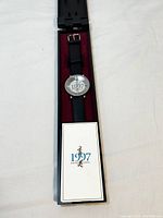 Wristwatch inside black presentation case with burgundy velvet lining and certificate card placed inside the case.