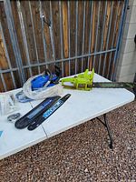 Photo showing the Green Blue Max gas chainsaw with attached chain and two additional Blue Max chain bars on table, some wear and rust visible on blade.