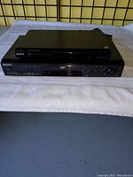 Front view of two black Sony DVD players stacked, showing control buttons, disc trays, and display windows.