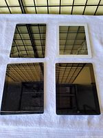Top-down view of four Apple tablets arranged in a grid on a white towel. Two tablets have black bezels and two have white or black bezels. Screens reflect overhead grid lights.