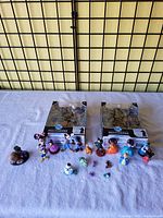 Photo showing two boxed DC Multiverse action figures: Superman and Robin King, and multiple small used Disney character figurines arranged on a cloth surface.