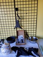 Photo showing ceramic Dalmatian snack jar, black rubber bowl, stainless steel bowl, Adidas dog suit, dog bridle/leash hanging on grid, and professional clippers in box.