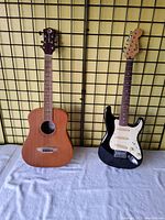 Both guitars side by side, Luna acoustic and Squire electric, shown on white cloth covering.