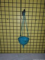Blue ceramic hanging planter suspended by blue chains on a grid background.