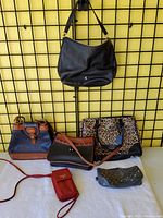 Front view of five purses arranged on a white surface, hanging on a grid wall behind, showing various colors and styles.