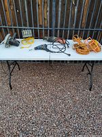 Wide view of all tools and extension cords on folding table outdoors on gravel surface