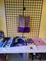 Purple patterned scarf hanging on a grid wall above the table of folded scarves and blanket.