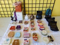 Photo showing an assortment of wax scent bars and melts from Scentsy and Gold Canyon, black Scentsy wax warmer, small round scented wax containers, and packaged wax cones.