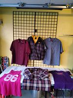 Six shirts and one jacket displayed hanging and laid on table, showing various colors and patterns.